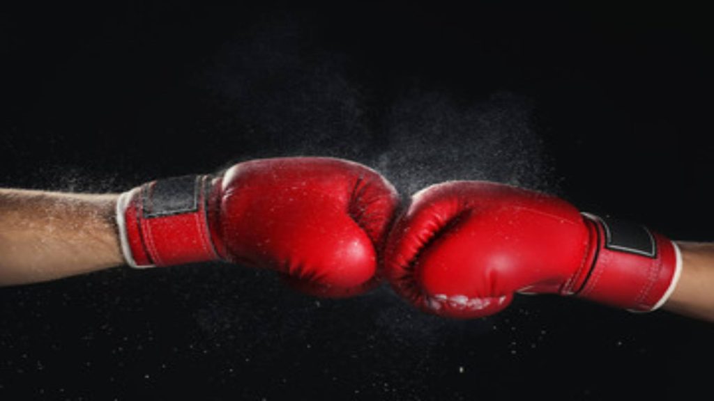 Cet image montre deux gants de boxe rouge qui se touche et il y a un fond noir en arrière plan.